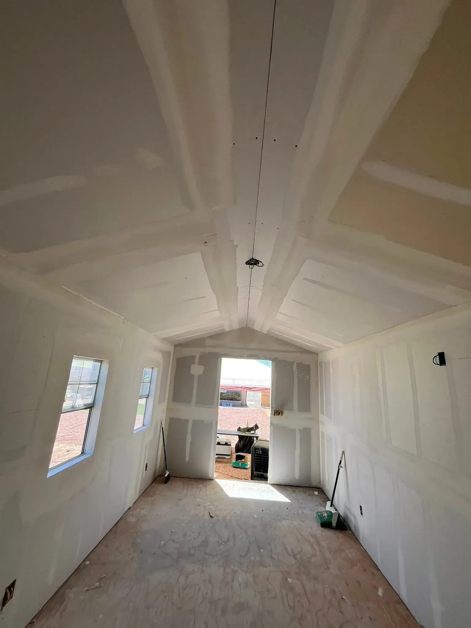 Drywall installation and finishing in progress inside a Tempe home with a vaulted ceiling and windows
