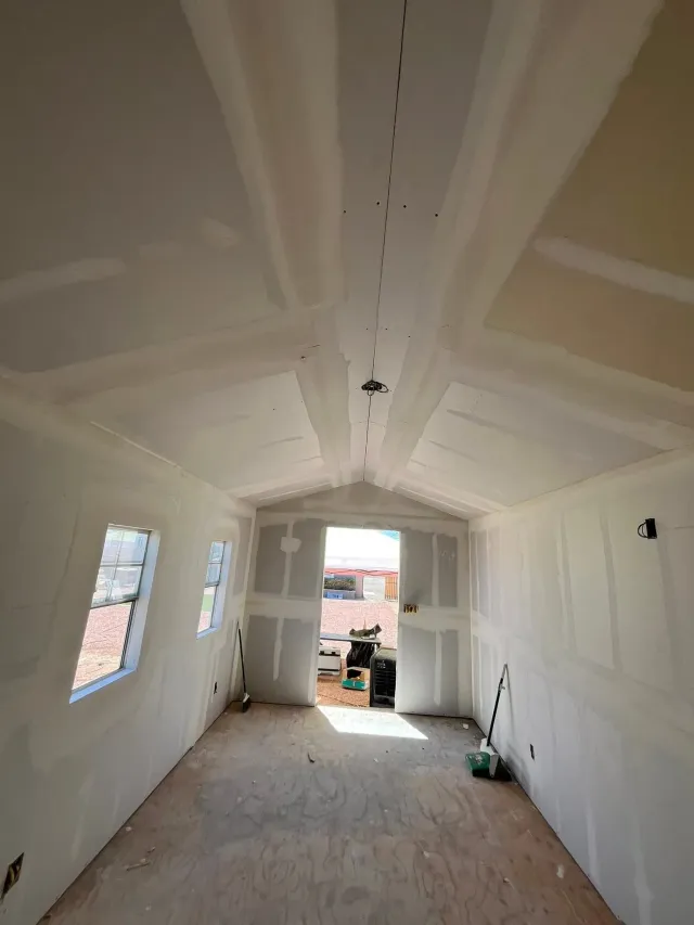 Drywall installation and finishing in progress inside a Tempe home with a vaulted ceiling and windows