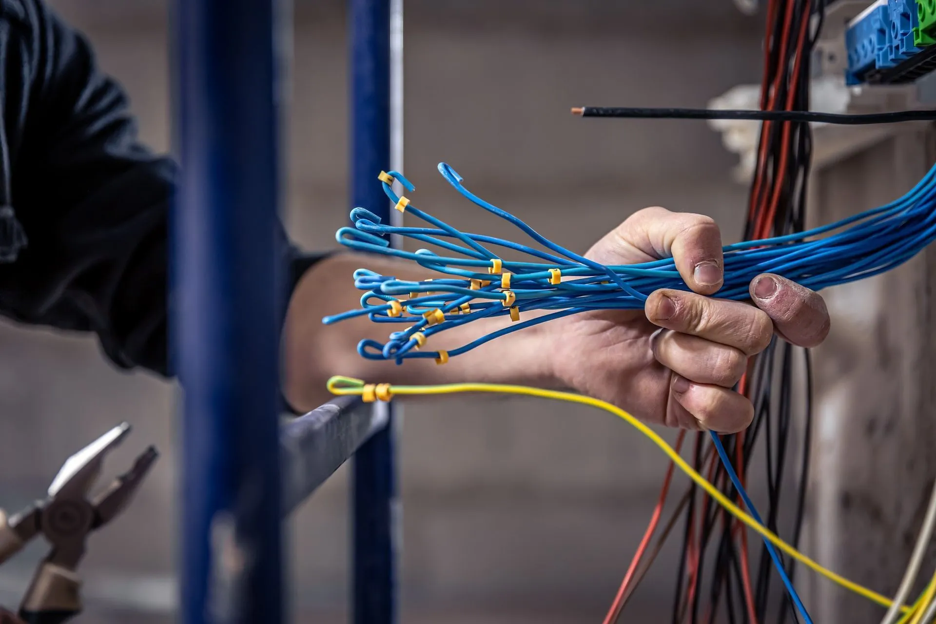 Hand pulling blue and yellow network cables in a wall-mounted wiring panel