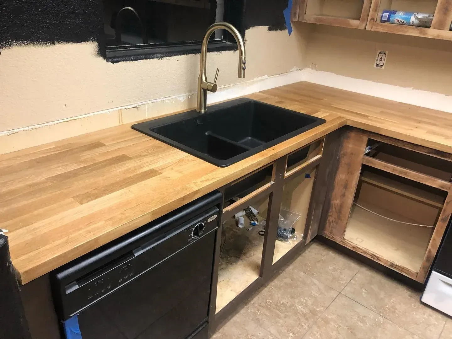 Modern kitchen counter with black sink, wooden countertop, and open cabinet space underneath.