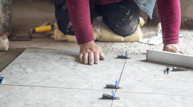 Worker aligning floor tiles with spacers and a trowel during installation work