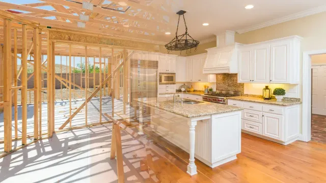 Bright kitchen with marble island, white cabinets, hardwood floors, and open framing under construction