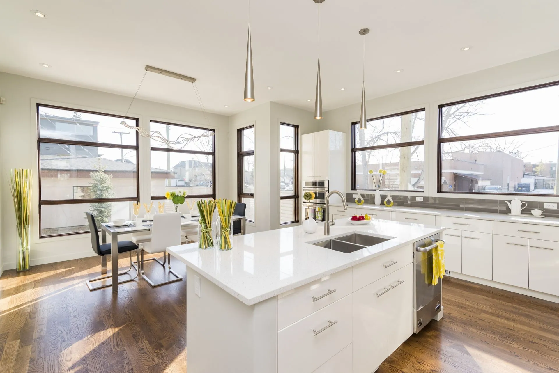 Bright modern kitchen with white island, pendant lights, large windows, and hardwood floors